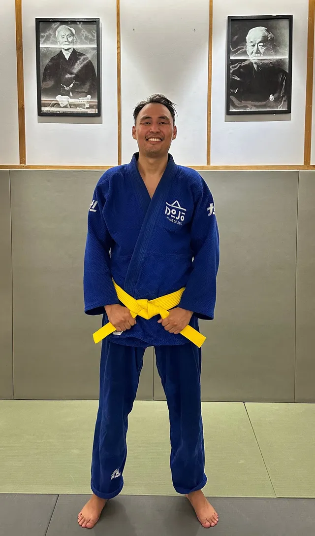 Simon standing on the mats of a dojo, wearing a blue judogi